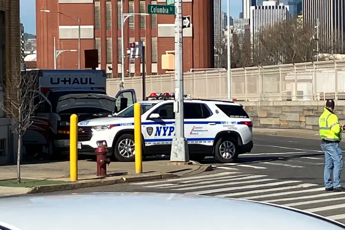 A sidewalk with the U-Haul truck and an NYPD car.